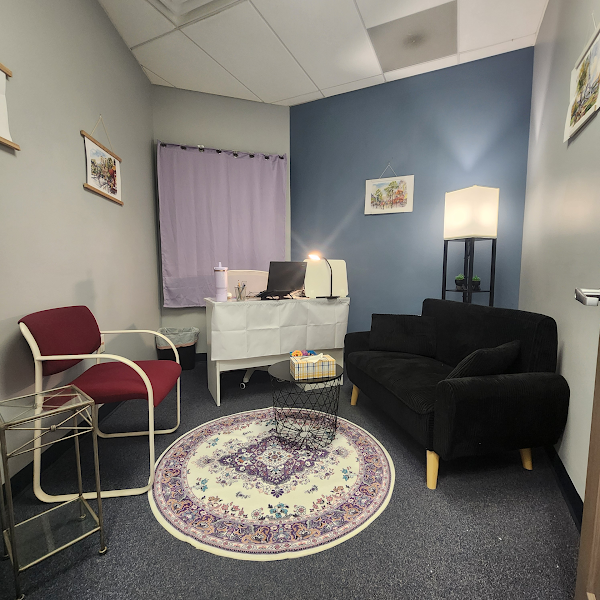Warm and inviting counseling office interior with lavender curtains, comfortable seating, plants, and soft natural light